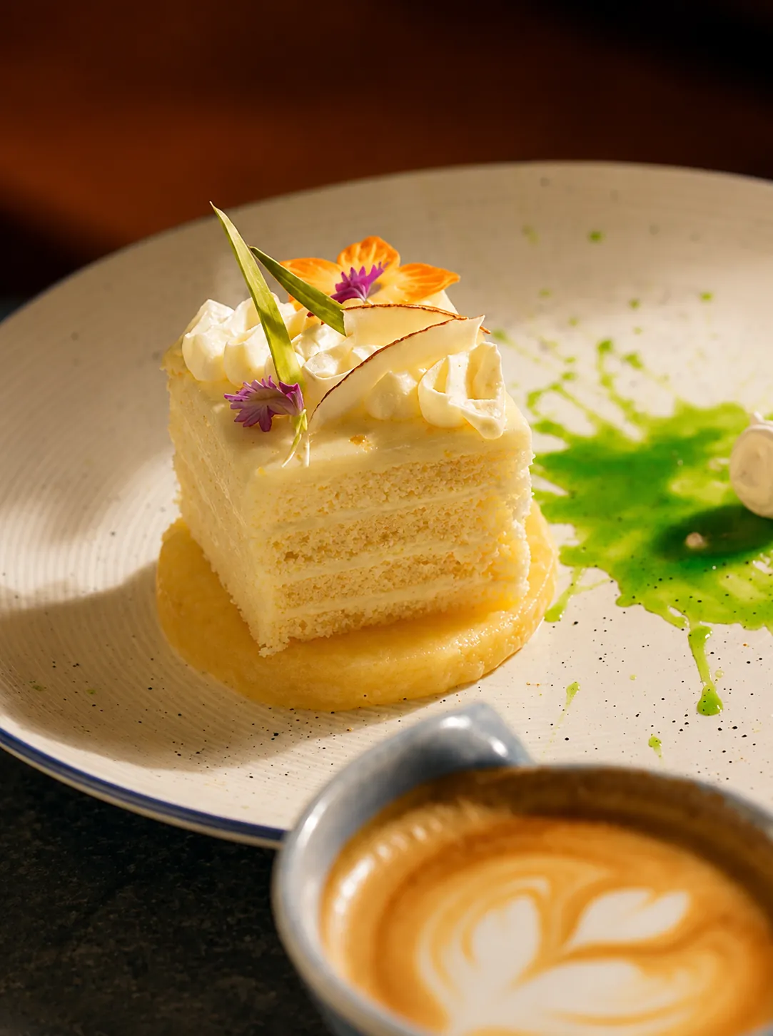 Layered vanilla cake slice served beside a latte