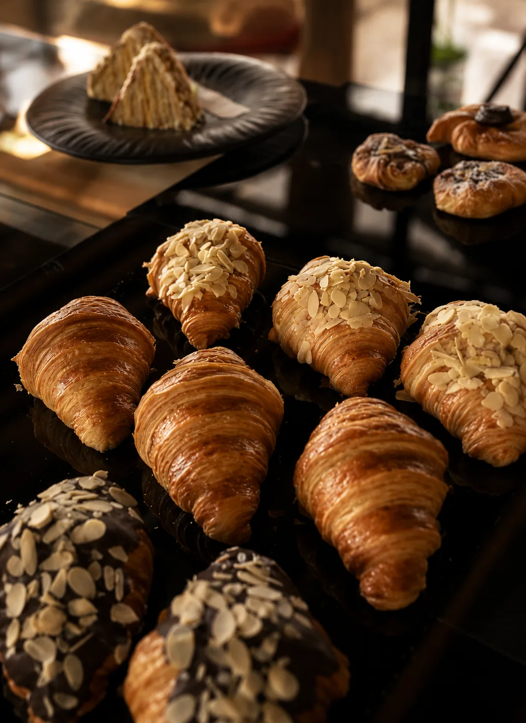 A tray of freshly baked butter croissants, some topped with sliced almonds and dark chocolate
