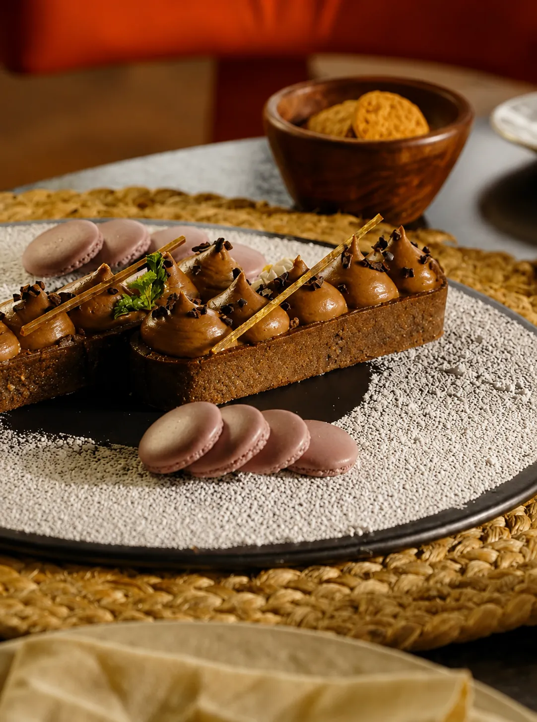 Chocolate tart with dark chocolate ganache, macarons and toasted honeycomb shard on a black plate